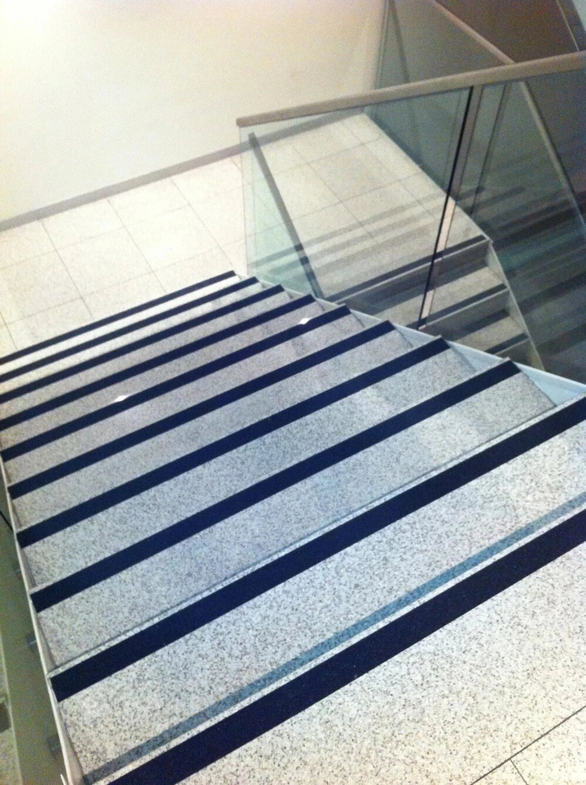 Anti-Slip Safety Tape on indoor marble stairs with glass railing - black grip strips on each step